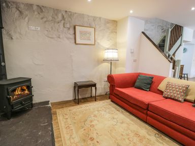 A sitting area with a red sofa, wood stove, floor lamp, small table, and floral rug at Stabla in Chwilog