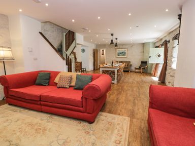 A living room with red sofas a wooden dining table and chairs wooden flooring and white stone walls at Stabla in Chwilog