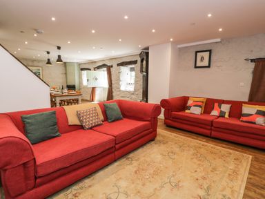 A living room with two red sofas and a dining table in the background at Stabla in Chwilog