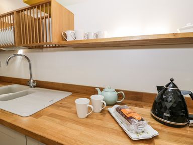 A kitchen counter with a sink mugs a teapot a loaf of bread and a kettle at Stabla in Chwilog