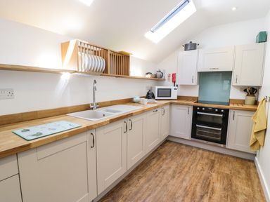 A kitchen with wooden countertops white cabinets a double sink an oven a microwave and a dish rack at Stabla in Chwilog