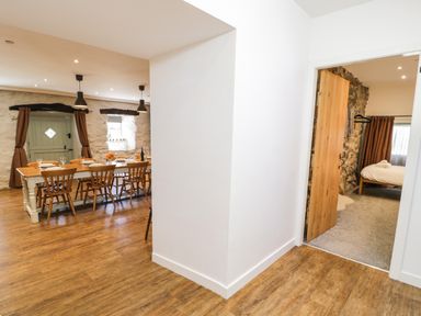 A dining area with a wooden table and chairs beside a room with a bed and stone walls at Stabla in Chwilog