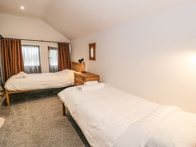 A bedroom with two single beds white linens a wooden bedside table with a lamp and two windows with curtains at Stabla in Chwilog