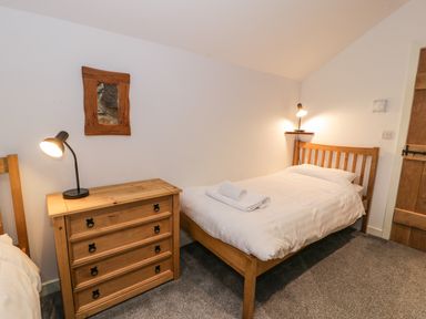 A bedroom with a single wooden bed, wooden chest of drawers with a lamp, and a wooden door at Stabla in Chwilog