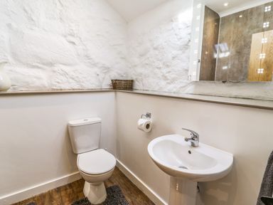 A bathroom with a toilet a sink a mirror and a basket on a shelf at Stabla in Chwilog