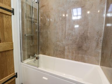 A bathroom with a bathtub shower enclosure and wooden door at Stabla in Chwilog