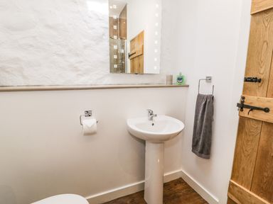 A bathroom with a pedestal sink a mirror a towel rack with a towel and a wooden door at Stabla in Chwilog