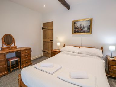 A bedroom with a double bed with white linens two bedside tables with lamps a wooden dressing table with mirror and stool and a painting on the wall at Stabla in Chwilog