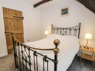 A bedroom with a metal bed frame white bedding wooden door bedside tables with lamps and a small framed picture on the wall at Stabla in Chwilog