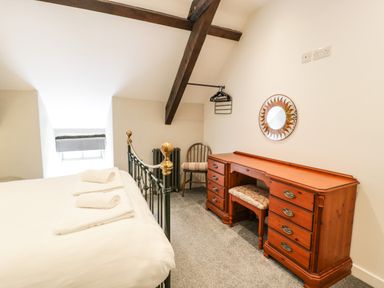A bedroom with a metal bed with towels a wooden dresser with a mirror and a chair with a cushion at Stabla in Chwilog