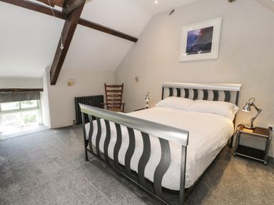 A bedroom with a metal bed frame a wooden chair bedside tables and a window at Stabla in Chwilog