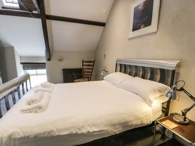 A bedroom with a bed with white sheets and towels a wooden chair and a bedside table with a lamp at Stabla in Chwilog