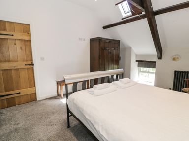 A bedroom with a bed with towels on it a wooden door a wooden wardrobe and a window under roof beams at Stabla in Chwilog