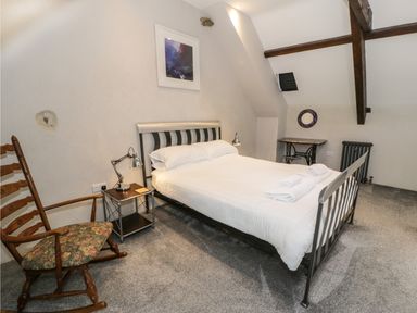 A bedroom with a metal frame bed a wooden rocking chair bedside table with lamp and towels on bed at Stabla in Chwilog