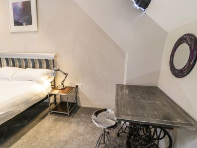A bedroom with a metal bed frame white bedding a bedside table with a lamp a metal desk with a stool and a round mirror on the wall at Stabla in Chwilog