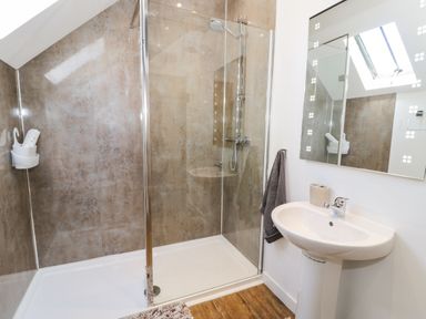 A bathroom with a glass shower enclosure a white sink with a towel and mirror at Stabla in Chwilog