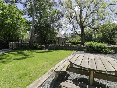 An outdoor garden area with a wooden picnic table trees and a stone wall at Stabla in Chwilog