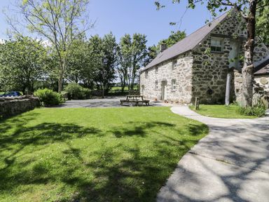 A stone cottage with a paved path and picnic table on a lawn with trees in the background at Stabla in Chwilog