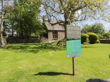 An outdoor grassy area with a 15th century stone house and a signpost with information at Penarth Fawr in Chwilog