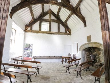 A room with wooden benches stone floor and a large fireplace at Stabla in Chwilog