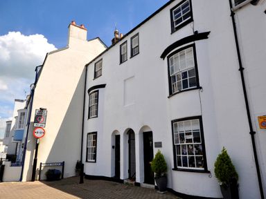 A street view of white buildings with black window frames and doors with plants outside at The Ferryman in Weymouth