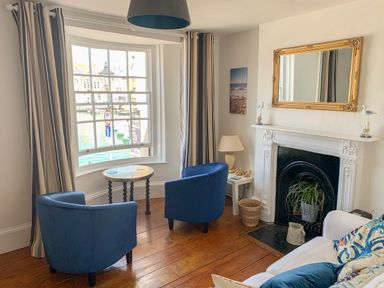 A seating area with two blue chairs a round table a white fireplace with a gold-framed mirror and a sofa with cushions at The Ferryman in Weymouth