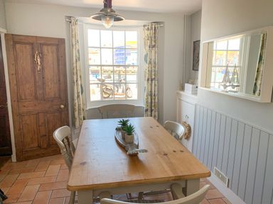 A dining room with a wooden table four chairs a window with patterned curtains and a wooden door at The Ferryman in Weymouth