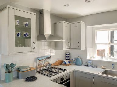 A kitchen with grey cabinets a gas stove a blue kettle and utensils at The Ferryman in Weymouth