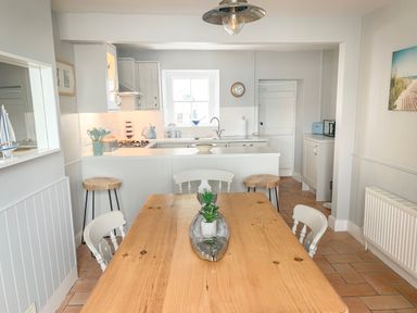 A kitchen and dining area with a wooden table and white chairs at The Ferryman in Weymouth