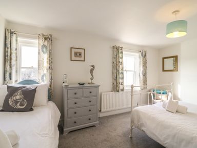 A bedroom with two single beds a gray chest of drawers and floral curtains at The Ferryman in Weymouth