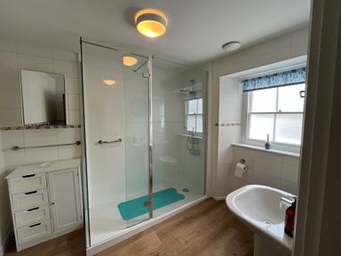A bathroom with a glass shower stall a white sink a small cabinet and a window at The Ferryman in Weymouth