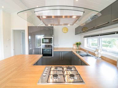 A kitchen with a gas stove on a wooden countertop and gray cabinets at Alder Lodge in Teigngrace near Newton Abbot