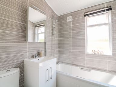 A bathroom with a white sink cabinet a toilet a bathtub with a glass shower screen and a window at Alder Lodge in Teigngrace near Newton Abbot