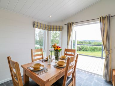 A dining area with a wooden table set for four near large windows and a sliding door opening to a garden at Birch Lodge in Teigngrace near Newton Abbot