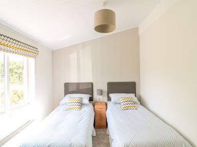 A bedroom with two single beds separated by a wooden nightstand with a lamp at Birch Lodge in Teigngrace near Newton Abbot