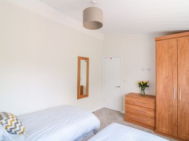 A bedroom with two single beds a wooden chest of drawers with flowers a wooden wardrobe and a mirror on the wall at Birch Lodge in Teigngrace near Newton Abbot