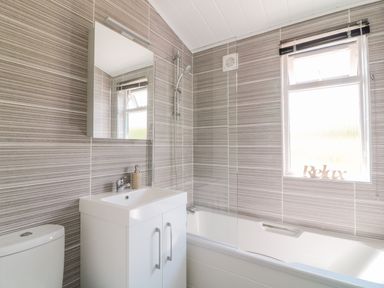 A bathroom with a toilet sink cabinet bathtub shower and a window at Birch Lodge in Teigngrace near Newton Abbot