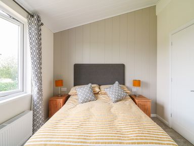 A bedroom with a double bed two bedside tables with lamps a window with patterned curtains and a closed door at Birch Lodge in Teigngrace near Newton Abbot