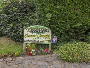 A sign for Twelve Oaks Farm Caravan and Camping Park surrounded by greenery and flowers