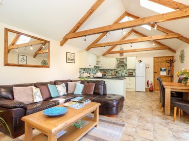 An open living room and kitchen with a brown leather sofa wooden coffee table and dining table with chairs at Valley View in St Martin near Mawgan