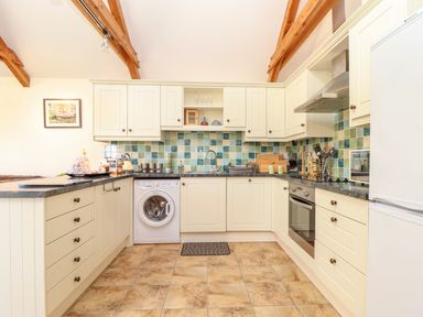 A kitchen with cream cabinets tiled backsplash and wooden beams at Valley View in St Martin near Mawgan