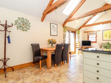 A dining area with a wooden table and four chairs next to a coat stand and a kitchen island at Valley View in St Martin near Mawgan