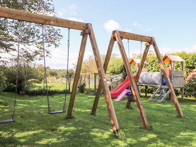 A playground with two wooden swings and a play structure with slides and climbing features on grass at Valley View in St Martin near Mawgan