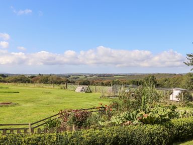 A garden with plants and a fence overlooking a grassy field and distant hills at Valley View in St Martin near Mawgan