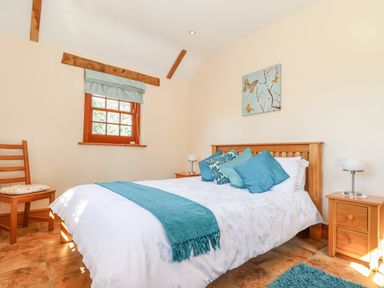 A bedroom with a wooden bed and blue cushions and throws with wooden nightstands and a window at Valley View in St Martin near Mawgan