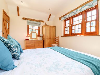 A bedroom with a bed blue pillows wooden dresser wardrobe and windows at Valley View in St Martin near Mawgan