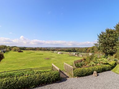 A garden with green grass a wooden gate and hedges overlooking fields and trees at Valley View in St Martin near Mawgan