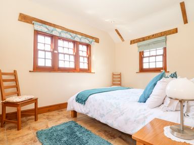A bedroom with a bed two wooden chairs a bedside table with a lamp and three windows at Valley View in St Martin near Mawgan