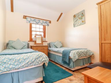 A bedroom with two single beds a wooden dresser with a mirror and lamps and a wardrobe at Valley View in St Martin near Mawgan