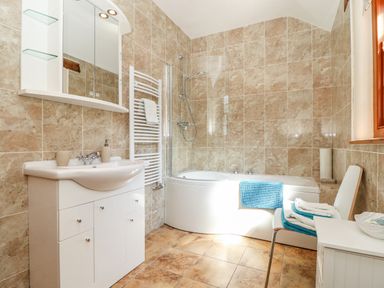 A bathroom with a white sink cabinet a bathtub with a shower a chair with towels and a window at Valley View in St Martin near Mawgan